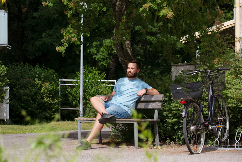 Henkilö istuu penkillä aurinkoisena, kesäisenä päivänä.