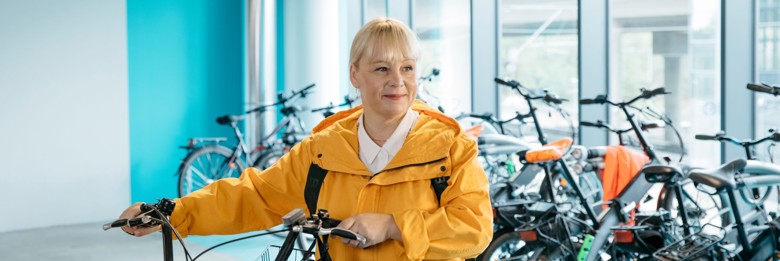 Nainen on pyörävarastossa ja pitää kiinni pyörän ohjaustangosta.